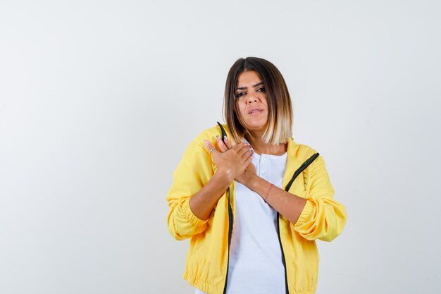 Vrouw handen houden op de borst in t-shirt, jas en op zoek verdrietig, vooraanzicht.