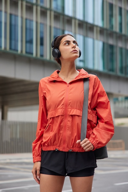 Gratis foto vrouw heeft buitentraining draagt fitnessmat om pilates-oefeningen te doen met instructeur loopt tegen stadsgebouw gekleed in activewear luistert naar liedjes uit afspeellijst