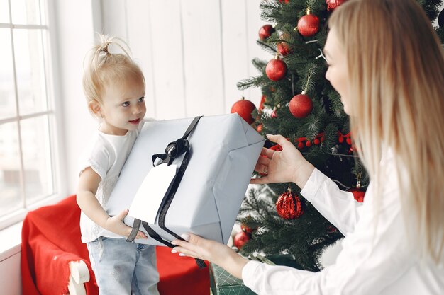 Vrouw heeft plezier met het voorbereiden van Kerstmis. Moeder in een wit overhemd speelt met haar dochter. Familie rust in een feestelijke kamer.