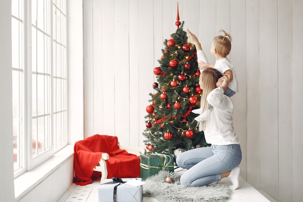 Vrouw heeft plezier met het voorbereiden van Kerstmis. Moeder in een wit overhemd speelt met haar dochter. Familie rust in een feestelijke kamer.