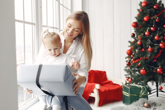 Vrouw heeft plezier met het voorbereiden van Kerstmis. Moeder in een wit overhemd speelt met haar dochter. Familie rust in een feestelijke kamer.