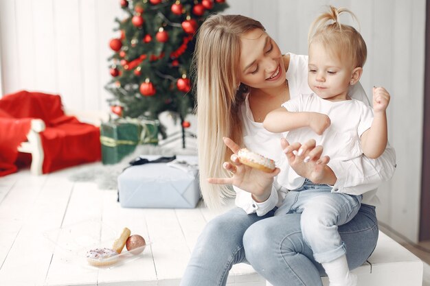 Vrouw heeft plezier met het voorbereiden van Kerstmis. Moeder in een wit overhemd speelt met haar dochter. Familie rust in een feestelijke kamer.