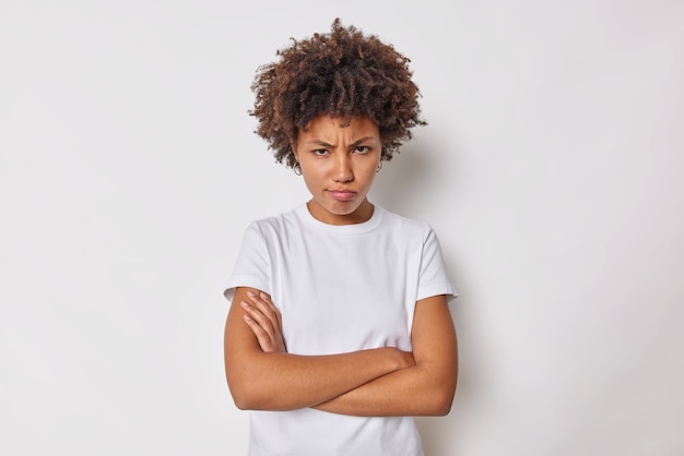 vrouw houdt armen gevouwen voelt zich beledigd of beledigd fronsen van onder het voorhoofd kijkt met ongeloof en belediging draagt casual t-shirt geïsoleerd op wit.