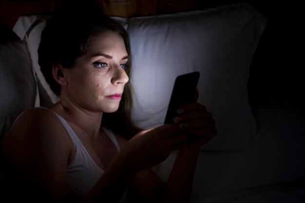 Vrouw houdt haar telefoon vast terwijl ze in bed ligt