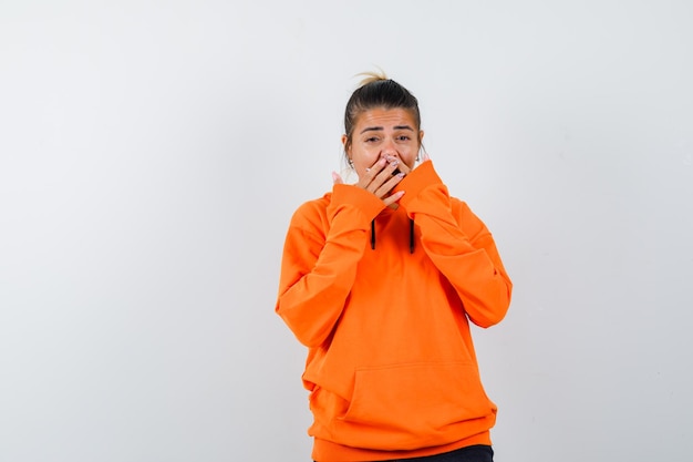 vrouw houdt handen op mond in oranje hoodie en ziet er vrolijk uit