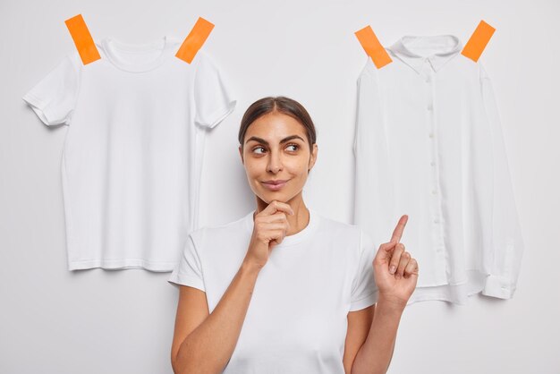 vrouw houdt kin wijst naar kledingstukken gekleed in casual t-shirt poses op wit