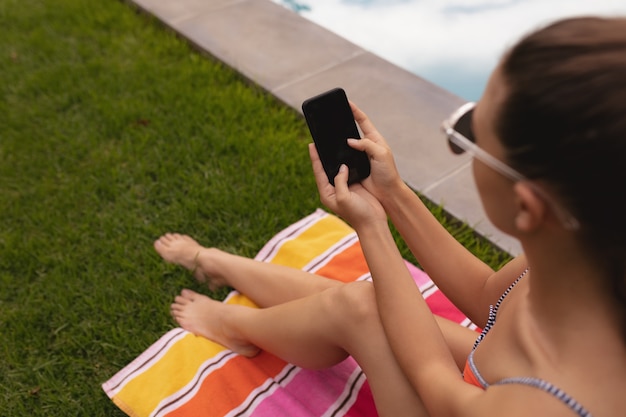 Vrouw in badmode met behulp van mobiele telefoon bij het zwembad