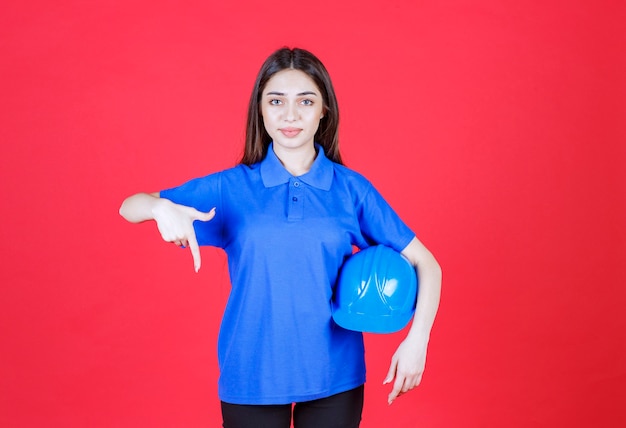 vrouw in blauw shirt met een blauwe helm en ergens in de buurt wijzend.