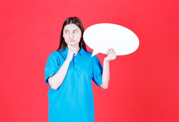 vrouw in blauw shirt met een ovale infobord en ziet er cofnused en attent uit.