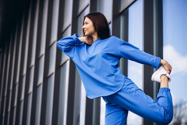 Vrouw in blauwe sportkleding die zich uitstrekt buiten de straat