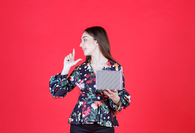 Vrouw in bloemenshirt met een zilveren geschenkdoos en ziet er attent uit.