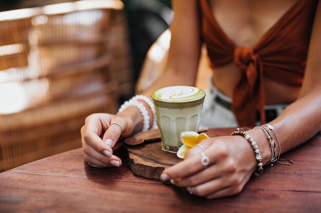 Vrouw in bruine beha zit in café en houdt glas met matcha latte