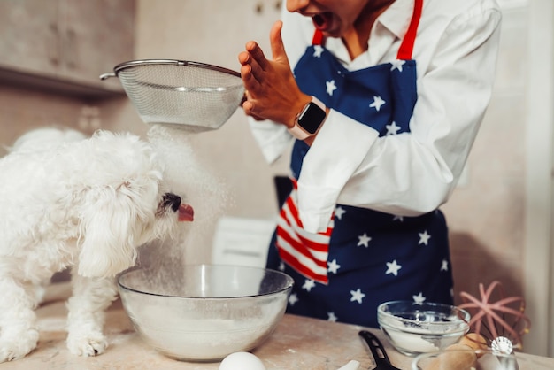 Gratis foto vrouw in de keuken zeeft bloem samen met een hond