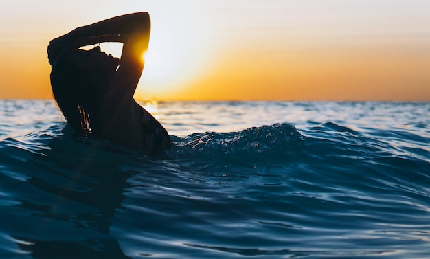 Vrouw in de oceaan in de zonsondergangtijd