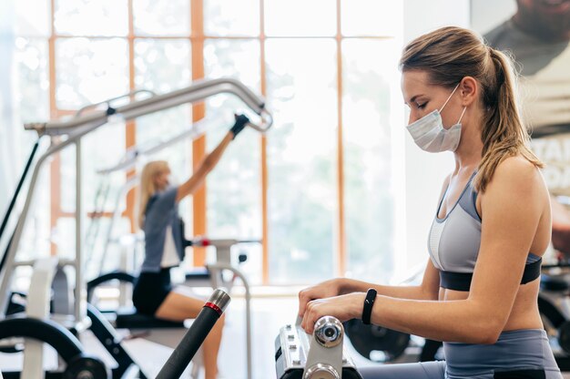 Vrouw in de sportschool met behulp van apparatuur met medisch masker