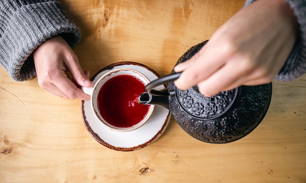 Vrouw in een café giet thee uit een zwarte gietijzeren theepot bovenaanzicht