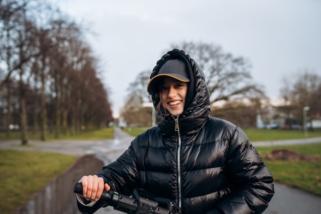 Vrouw in een jas op een elektrische scooter in een herfstpark. Rijden op elektrische voertuigen bij koud weer.