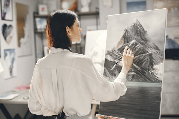 Vrouw in een kunstacademie die een schort draagt die op een ezel trekt.