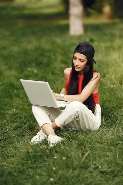 Vrouw in een lentestad. Dame met een laptop. Meisje zittend op een gras.