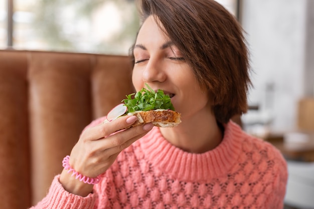 Vrouw in een restaurant in een gezellige warme trui gezond ontbijt met toast met rucola en zalm