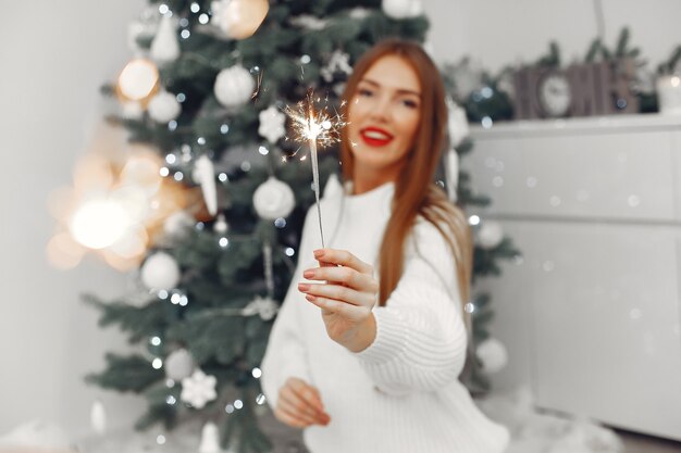 Vrouw in een witte sweater die bij de kerstboom zit