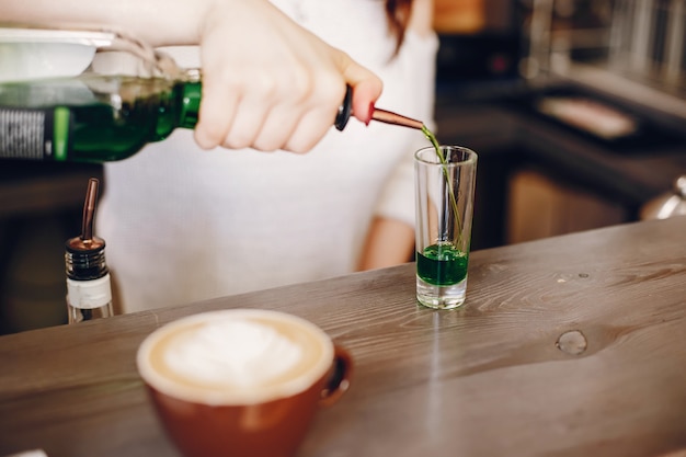 Vrouw in een witte sweater die groene syrop giet in glas