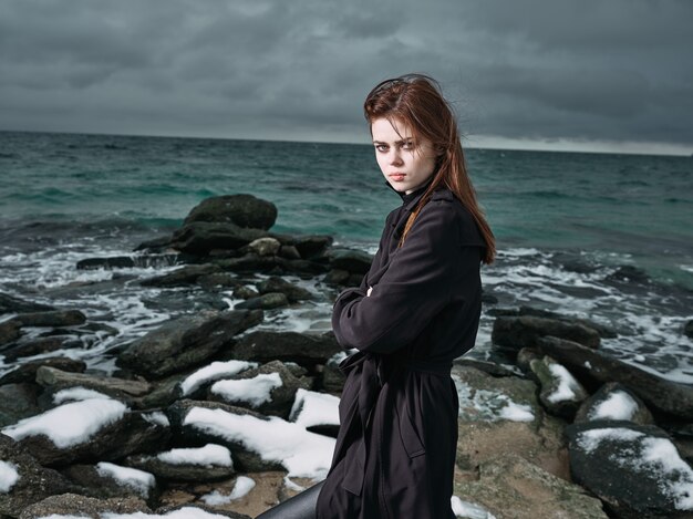 Vrouw in een zwarte jas buitenshuis landschap oceaan donkere wolken gothic