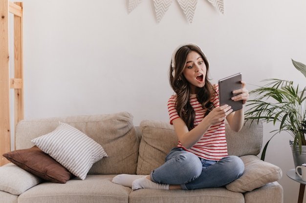 vrouw in enorme koptelefoon kijkt emotioneel en verbaasd naar het scherm van de tablet