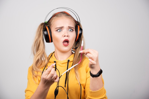 Vrouw in geel sweatshirt die koorden van hoofdtelefoons bekijkt.