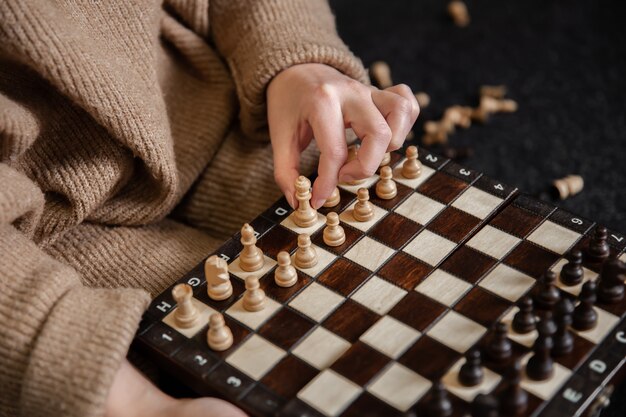 Vrouw in gezellige trui plaatst houten schaakstukken op een schaakbord.