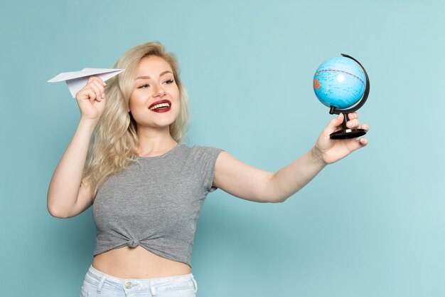 vrouw in grijs shirt en heldere blauwe spijkerbroek holdign papieren vliegtuigje en kleine wereldbol