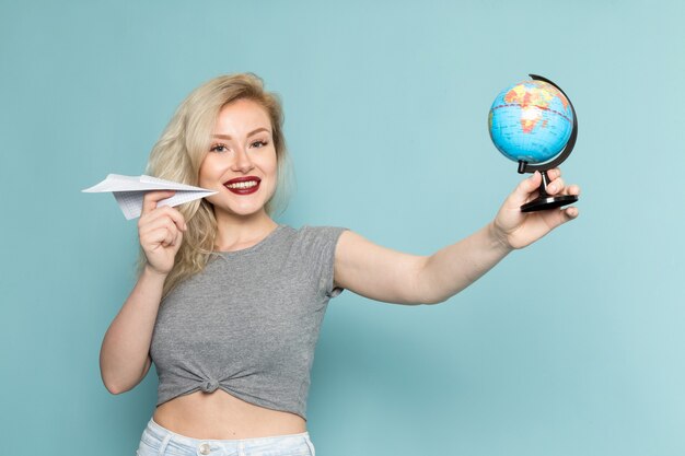 vrouw in grijs shirt en heldere blauwe spijkerbroek met papieren vliegtuigje en kleine wereldbol