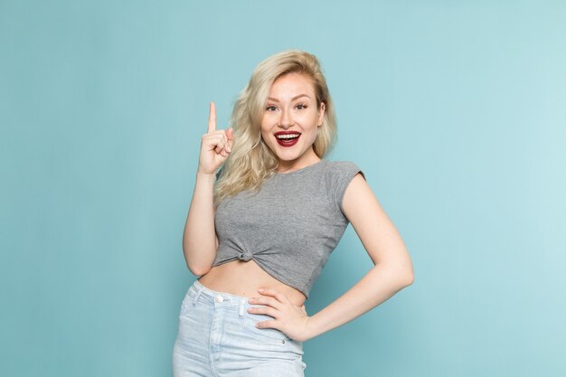 vrouw in grijs shirt en heldere blauwe spijkerbroek poseren met een glimlach