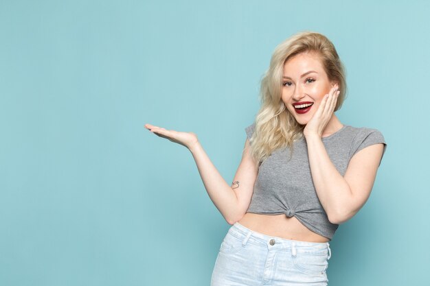 vrouw in grijs shirt en heldere blauwe spijkerbroek poseren met opgetogen uitdrukking