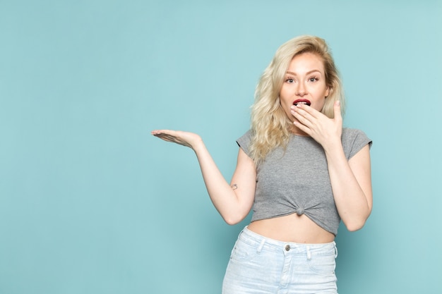 Vrouw in grijs shirt en heldere blauwe spijkerbroek poseren met verbaasde uitdrukking