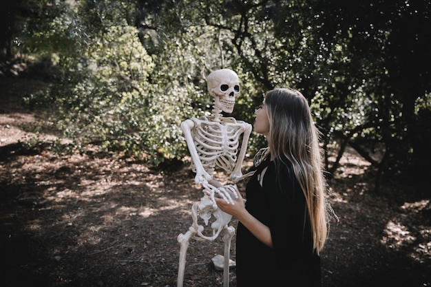 Vrouw in heksenkostuum die en aandachtig skelet houden kijken