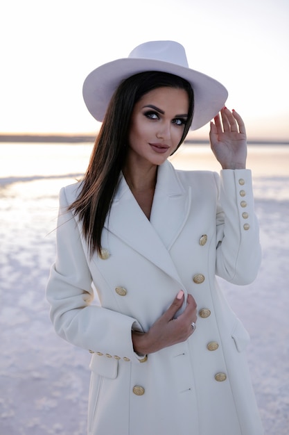 Vrouw in het wit Vrouwen met winterschoenen Europees meisje in jas lachend op een koude dag Vrolijke blonde vrouw met plezier tijdens winter fotoshoot winter meer over sneeuw warme laarzen Hoed