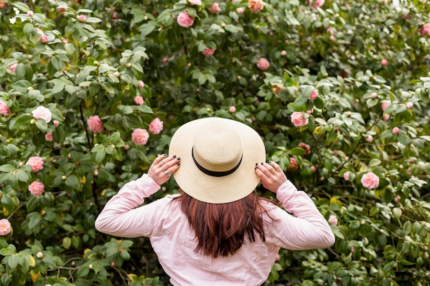 Gratis foto vrouw in hoed dichtbij roze bloemen die op groene takjes groeien