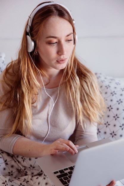 Gratis foto vrouw in hoofdtelefoons die laptop in bed met behulp van