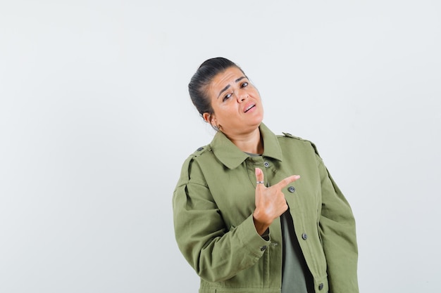 vrouw in jasje, t-shirt wijst naar rechts en kijkt trots