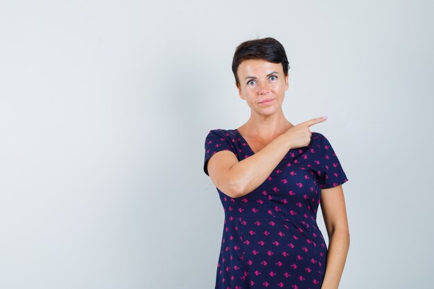 Vrouw in jurk die naar de rechterkant wijst en er verstandig uitziet