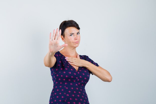 Vrouw in jurk met stopgebaar en op zoek geïrriteerd