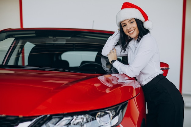 Vrouw in kerstmuts bij de rode auto in een autoshowroom