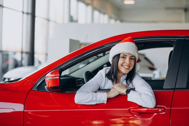 Vrouw in kerstmuts bij de rode auto in een autoshowroom