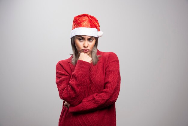 Vrouw in kerstmuts staande boos op grijze achtergrond.