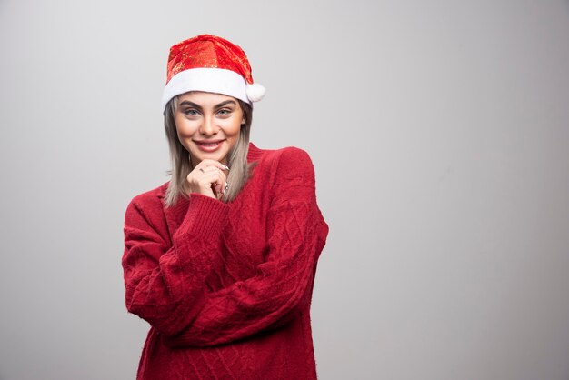 Vrouw in kerstmuts staat gelukkig op een grijze achtergrond.