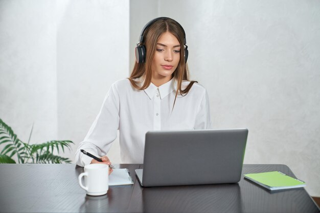 Vrouw in koptelefoon die laptop gebruikt om thuis te studeren