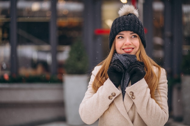 Gratis foto vrouw in laag die zich buiten de koffie in een de winterstraat bevindt