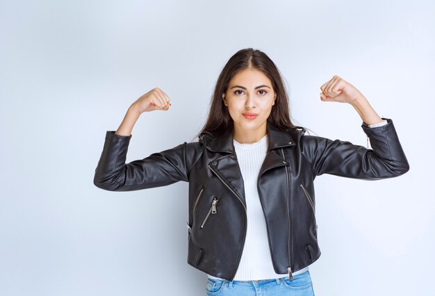 vrouw in leren jas die haar armspieren demonstreert.