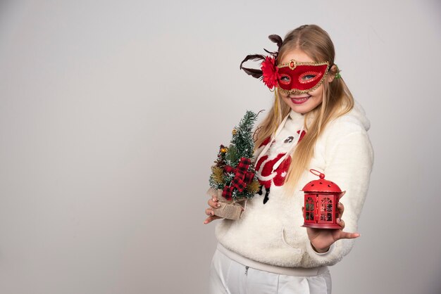 Vrouw in maskerademasker met cadeau en dennenboom.